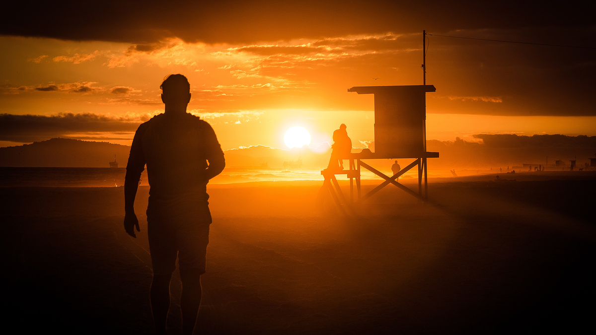 Summer Sunset Man Shorts Beach Sea Ocean Мужчина идет по пляжу на закате солнца сбоку смотровая вышка спасателей