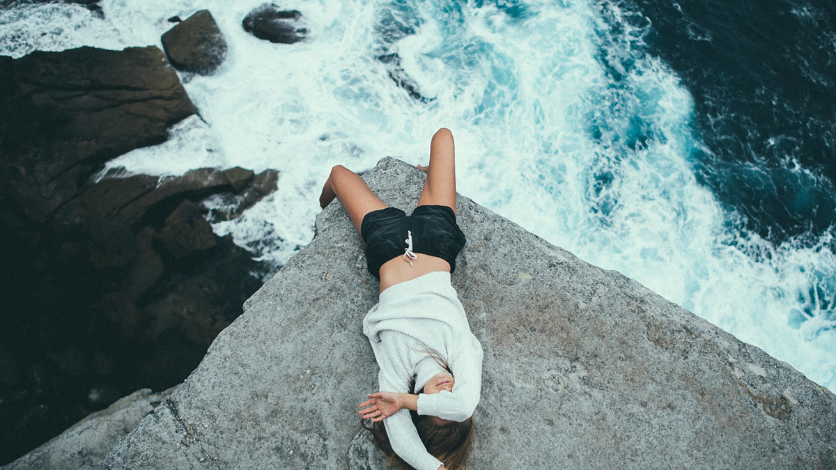 Woman Lags Rock Sea Ocean Blue Девушка в джемпере лежит на камне скалы свесив ноги внизу на фоне морского прибоя и волн прикрывая лицо рукой