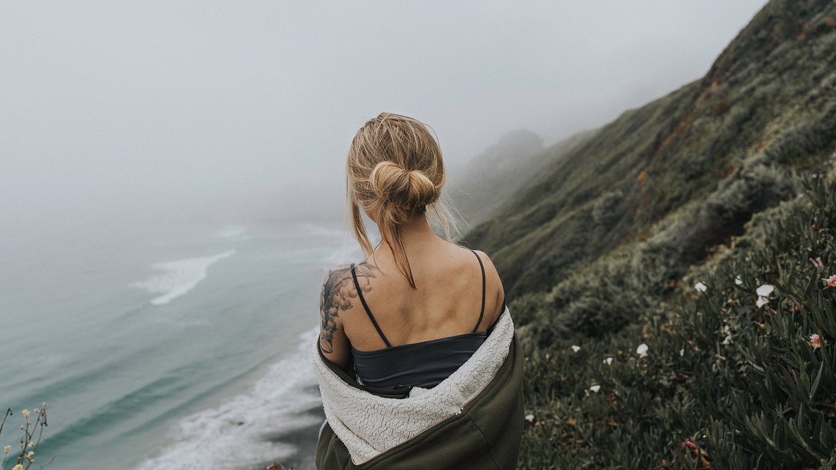 Woman Mountain Rock Fog Mist Ocean Sea Девушка с татуировкой на плече стоит на склоне горы и смотрит в сторону неба внизу морские волны